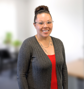 Staff photo of a young light-skinned black woman with dark hair up in a bun, wearing a red shirt and gray cardigan.