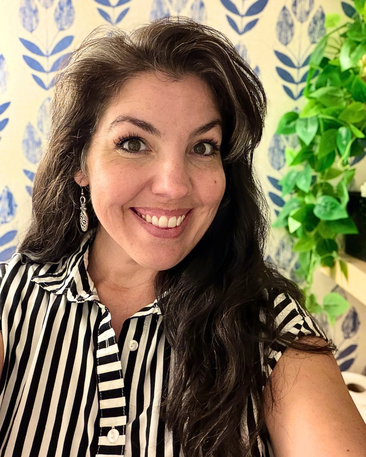 Female with long dark hair wearing a black and white striped blouse is smililing at the camera