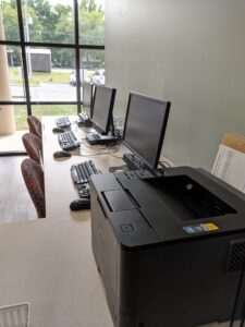 3 desktop computers and a printer sitting on a conference style table in a lobby