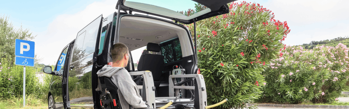 A young adult male wearing a grey hoodie jacket boards an accessible van while seated in his wheelchair